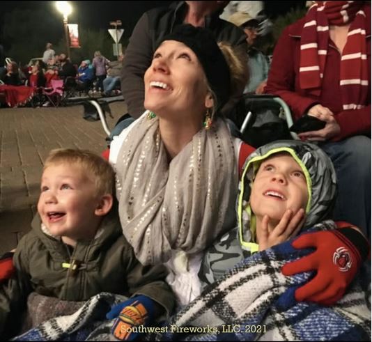 Family looking up in wonder at a Southwest Fireworks display Mother and two young sons wrapped in a blanket smiling and looking up at a fireworks display on a cool evening in a crowd of seated spectators